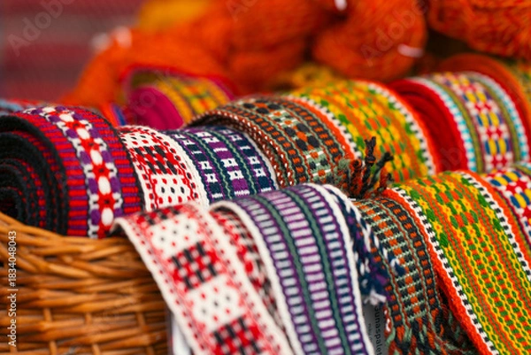 Fototapeta Close-up of colorful handwoven traditional belts displayed in a basket, highlighting their intricate patterns and vibrant colors.