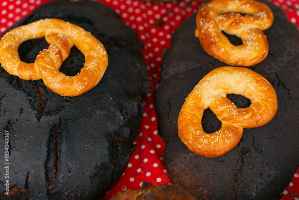 Fototapeta Traditional dark bread loaves topped with golden baked pretzels, displayed on a red polka-dot cloth.