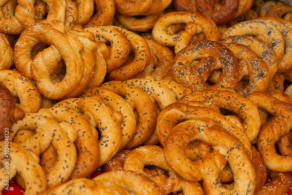 Fototapeta A pile of freshly baked pretzels with various seed and spice toppings, displayed at a market stall.
