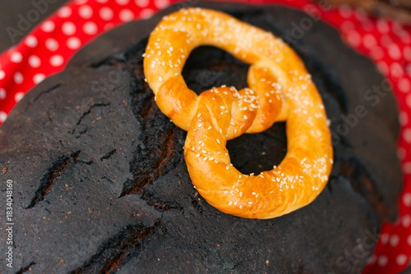 Obraz Traditional dark bread loaves topped with golden baked pretzels, displayed on a red polka-dot cloth.