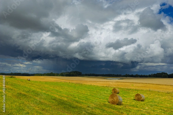 Obraz Dramatic rural landscape with hay bales on a field and dark storm clouds approaching across the countryside