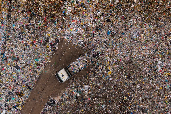 Obraz Aerial view of a waste truck unloading garbage at a landfill surrounded by massive amounts of mixed plastic and debris.