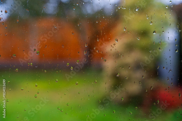Fototapeta Raindrops on the window with a bokeh garden background during late Autumn or Fall