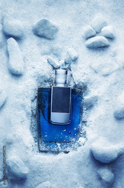 Fototapeta A bottle of fragrance is placed inside ice and snow. The setting shows a mix of icy surfaces and natural stones. The scene captures a moment of cold beauty.