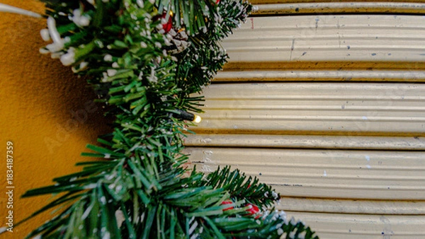 Fototapeta Close-up of artificial Christmas garland decorating the facade of a house. Festive synthetic pine branches with holiday ornaments and lights.