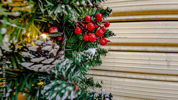 Fototapeta Close-up of artificial Christmas garland decorating the facade of a house. Festive synthetic pine branches with holiday ornaments and lights.