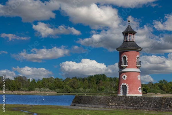 Fototapeta Historical Moritzburg Lighthouse on the Castle Pond under a dramatic blue sky with white clouds. Red facade and dark roof building