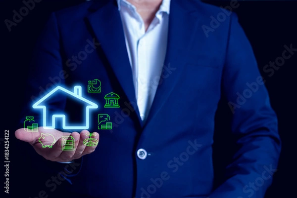 Fototapeta Businessman holding smart home icon with digital finance and property investment symbols, representing modern real estate technology.