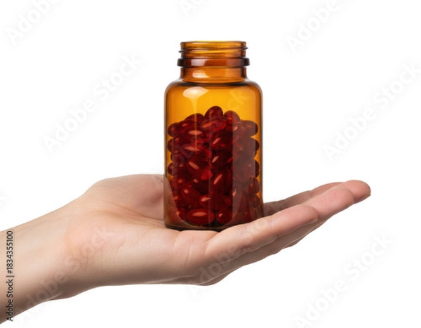 Obraz Hand holding an amber glass bottle filled with red softgel capsules against a deep, solid hue