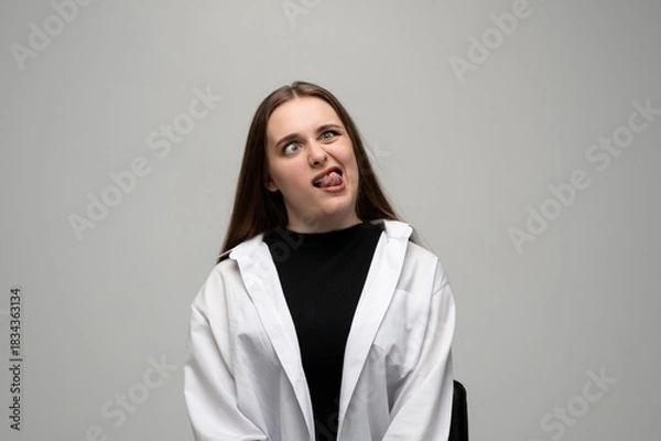 Fototapeta Woman making goofy sideways look with tongue out in humorous expressive studio portrait