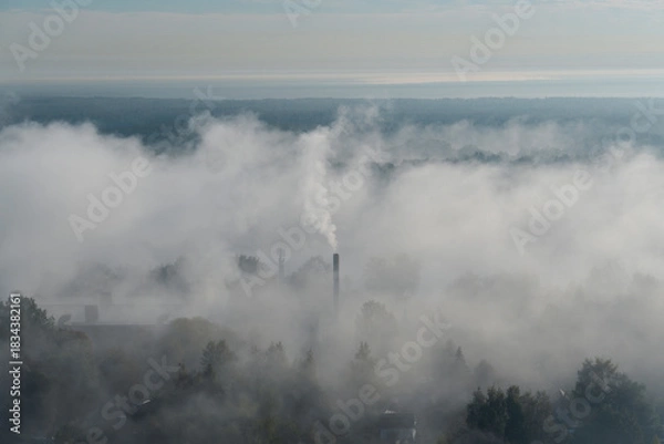 Obraz Fog covers the area while smoke rises from factory stacks. The scene captures an industrial landscape shrouded in mist during early morning hours