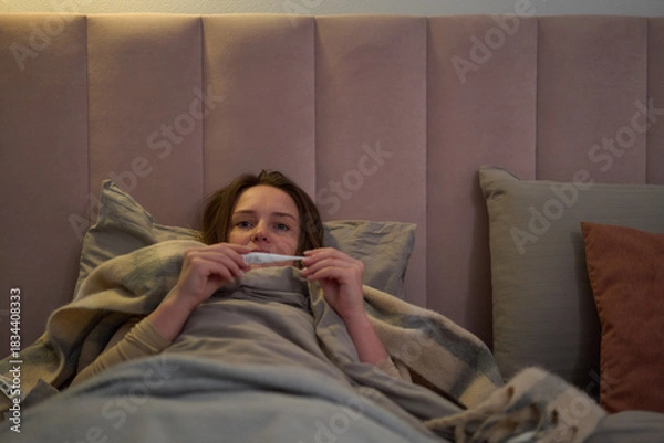 Obraz Female lying in bed checking thermometer while resting