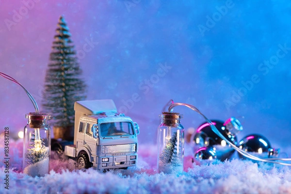 Fototapeta A toy truck is carrying a Christmas tree, a snow background with a garland and balloons. Copy space