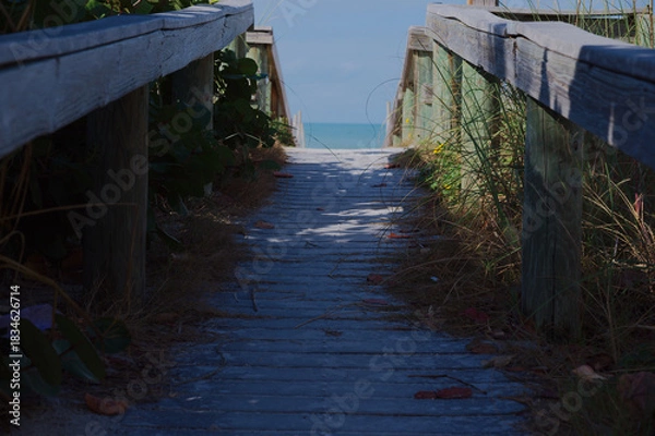 Obraz Sunny Beach Path With Weathered Wooden Railings Leading To Quiet Sea View at St. Pete Beach, FL. Sandy path opening to a calm blue sea. Ideal for travel, coastal lifestyle, relaxation, and nature them