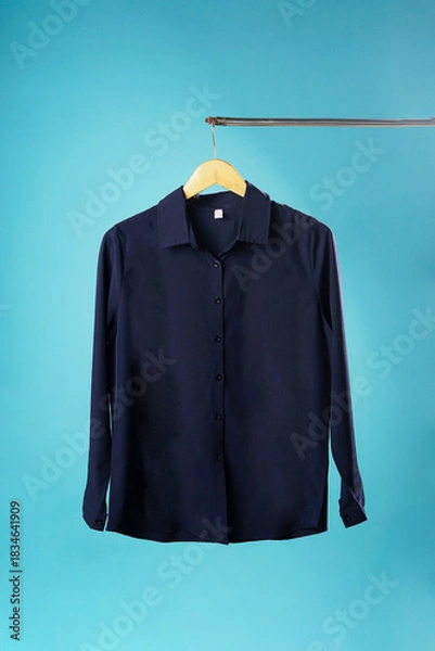 Fototapeta A navy-colored shirt hangs neatly on a hanger against a bright blue background