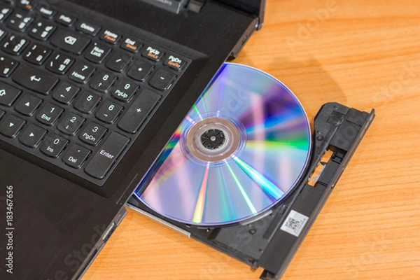 Fototapeta DVD ROM inserted in laptop computer on wooden texture background