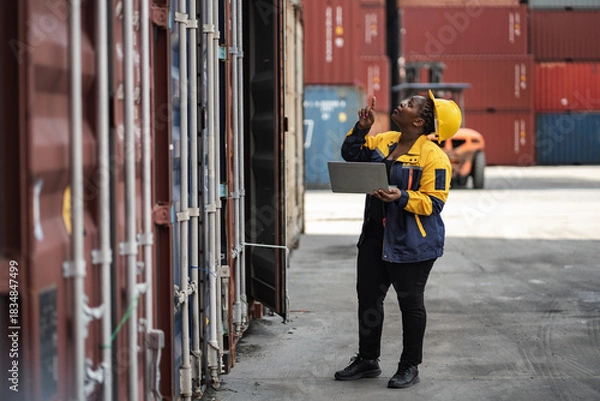 Obraz African woman logistics workers use notebook computer checking container	