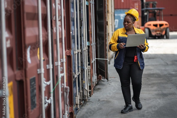 Obraz African woman logistics workers use notebook computer checking container	