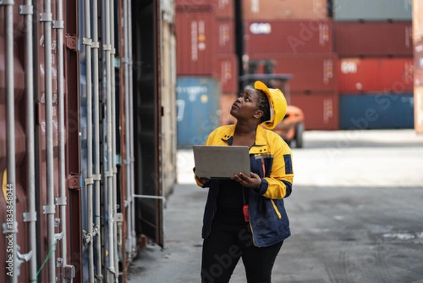 Obraz African woman logistics workers use notebook computer checking container	
