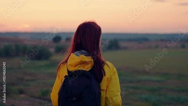 Fototapeta Lonely woman with backpack walks to empty farm field at sunset light. Woman traveler with backpack spend weekend in autumn park. Sportswoman on tour to wild nature at calm autumn evening twilight