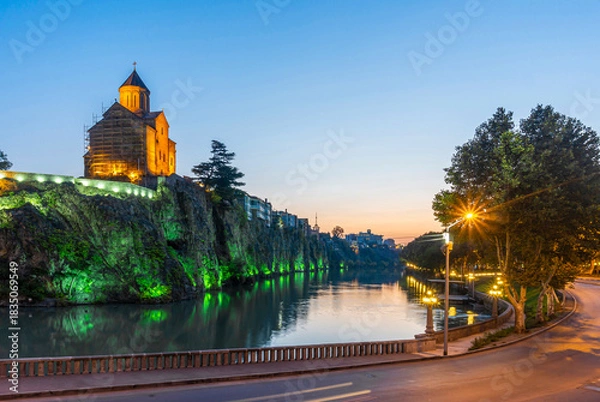Obraz Night view of the old district of Tbilisi. The church and rocks are reflected in the Kura River and illuminated with colored lights. Blue sky.