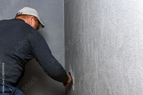 Fototapeta Worker using a float to smooth decorative pebble plaster on a wall.
