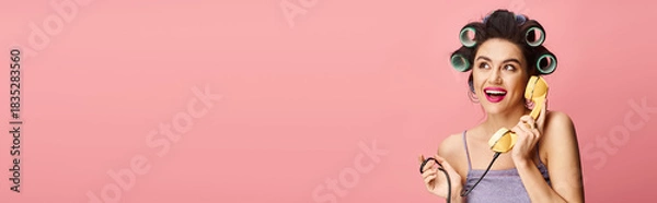 Obraz Beautiful young woman in curlers enjoying a cheerful phone call against a pink background