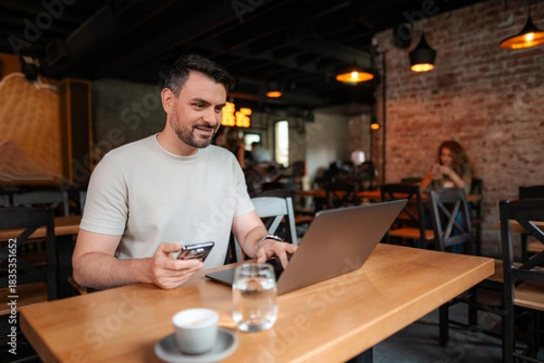 Fototapeta Young businessman using laptop and smartphone in a cafe