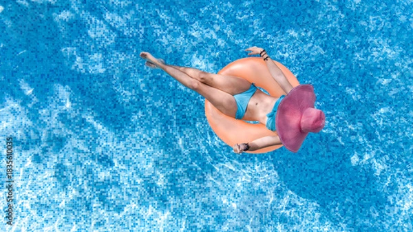 Fototapeta Aerial drone view of beautiful woman in hat relaxing in swimming pool, young girl in bikini swims on inflatable ring donut and has fun in blue pool water, tropical vacation on holiday resort