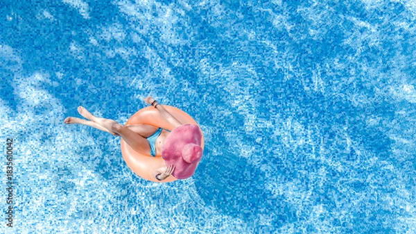 Fototapeta Aerial drone view of beautiful woman in hat relaxing in swimming pool, young girl in bikini swims on inflatable ring donut and has fun in blue pool water, tropical vacation on holiday resort