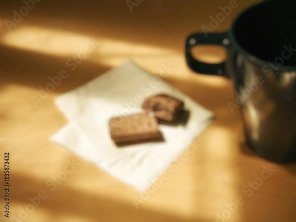 Fototapeta Blurred image of a simple aesthetic breakfast menu. Blurred image of a cup and a piece of chocolate biscuit on a table with patterned sunlight.