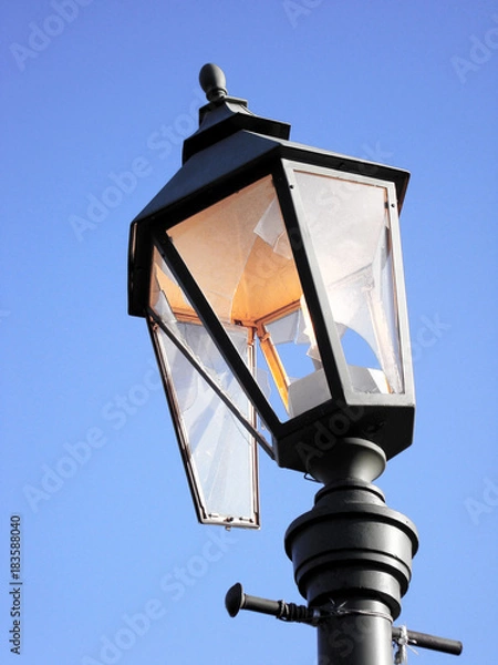 Fototapeta Streetlight burning during the day as a symbol of waste, losses and vandalism. Broken hooligans street lamp.