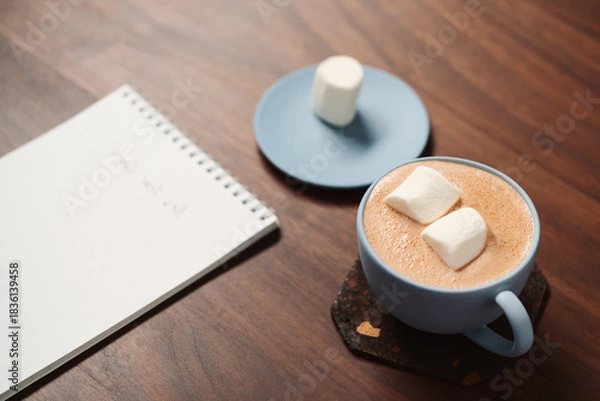 Obraz Hot chocolate in a blue cup with marshmallow and notepad on walnut table
