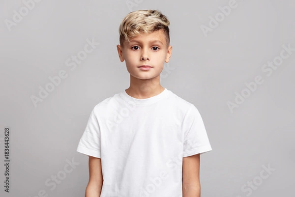 Obraz Portrait of blonde boy with stylish haircut standing in studio on gray background, calm child model looking at camera, neutral expression, clean beauty and fashion
