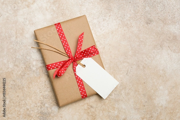 Obraz Blank gift tag mockup attached to a beautifully wrapped present with red polka dot ribbon, showcasing a rustic design ideal for personalized gifting and creative projects