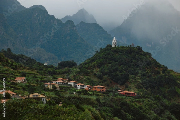Obraz Scenic view of a mountainous landscape featuring lush greenery, quaint houses nestled on hillsides, and a striking white church perched atop a peak, creating a serene atmosphere