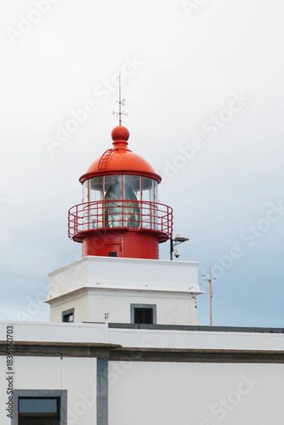 Obraz Red and white lighthouse structure with a prominent lantern, standing tall against a cloudy sky, symbolizing guidance and safety for maritime navigation