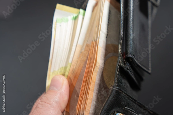 Fototapeta Hand holds an open black leather wallet packed with euro banknotes. Close-up view suggests cash payment, budgeting, and financial security.