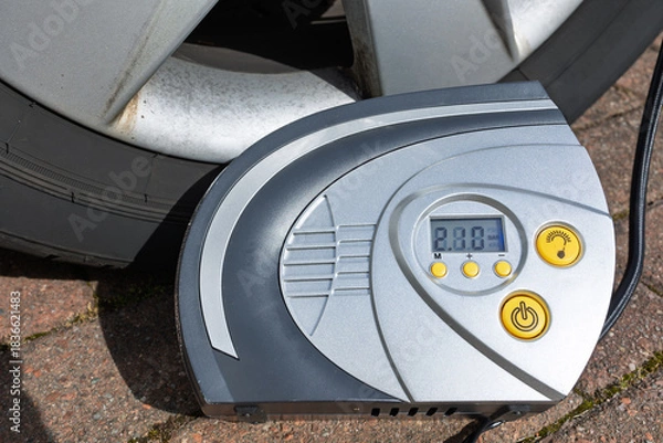 Fototapeta Close-Up of Digital Portable Tyre Inflator Beside Car Wheel