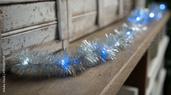 Fototapeta Silver tinsel garland with glowing blue lights on a rustic wooden shelf