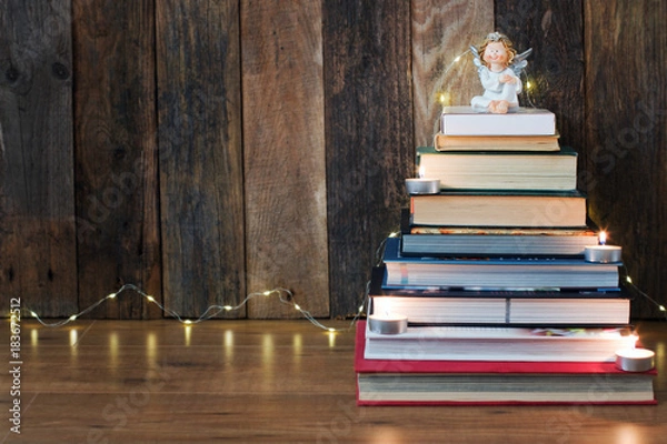 Fototapeta Christmas background with a pile of books, an angel, candles and a fir-tree garland