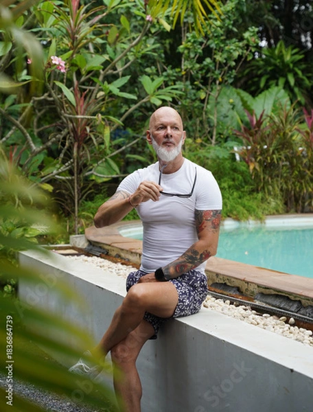 Obraz A man is comfortably sitting near a swimming pool in tropical area