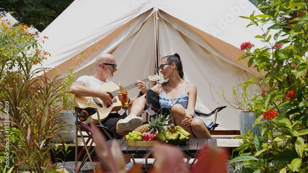 Obraz A man and woman is joyfully drinking beer and playing guitar near a cozy tent at glamping