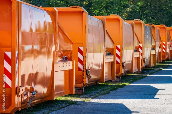 Fototapeta Multiple orange recycling bins lined up in a neat row at a waste management facility on a clear day