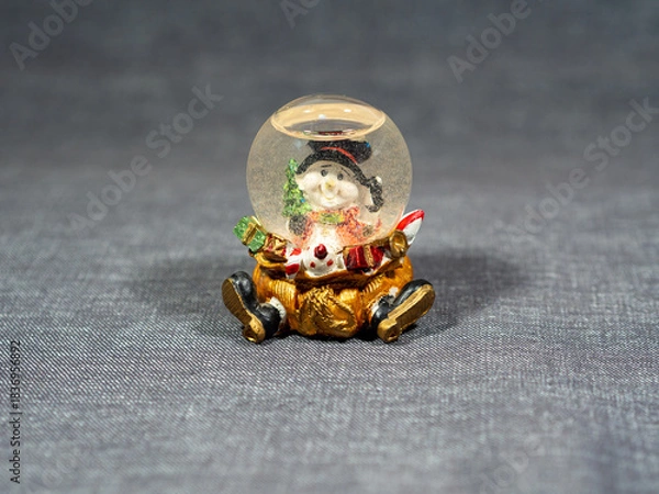 Fototapeta Snow globe with snowman and gift bag. Christmas decor element. Glass snow ball on a shelf or on a table