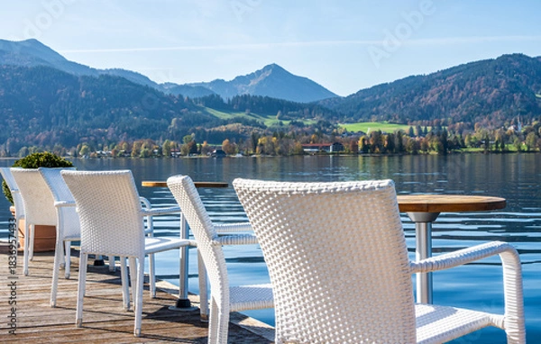 Fototapeta Relaxing seating arrangement by the calm lake with white chairs and a round pot in the morning sunlight