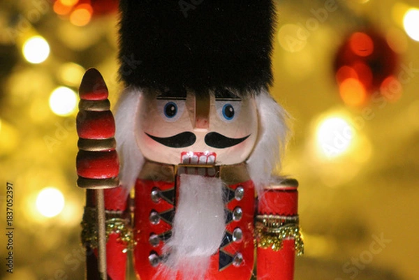 Obraz Close-up of a classic wooden nutcracker soldier in festive red uniform, set against warm holiday lights.