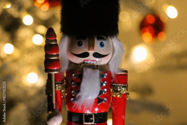 Obraz Wooden nutcracker guard with bright colors and fluffy hat photographed in front of glowing Christmas lights.