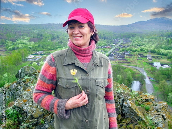 Fototapeta A beautiful mature woman holds a snowdrop in her hands against the backdrop of the South Ural Mountains on a spring day