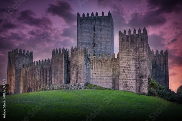 Obraz Sunset view of Guimaraes Castle in Portugal, featuring the medieval fortress under a dramatic purple sky during the golden hour.